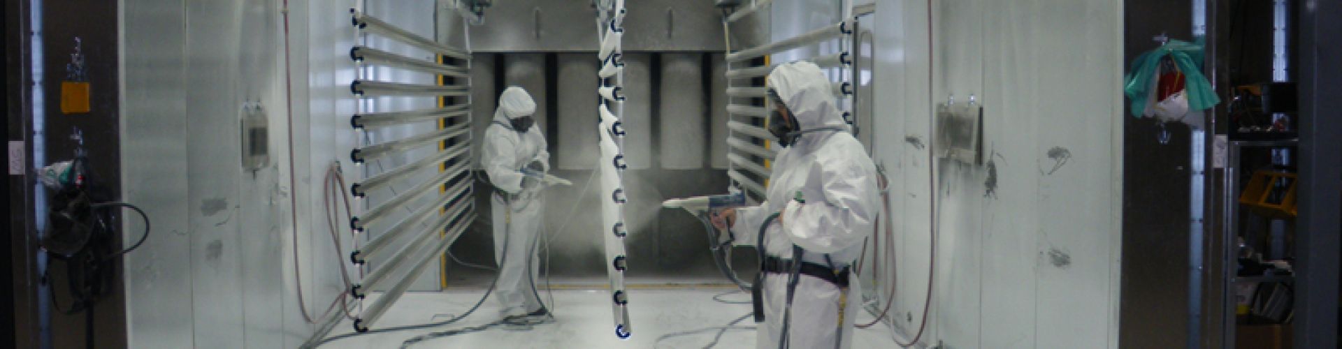 Two DekSmart staff in white PPE powder coating a set of aluminium railings in the powder coating booth.