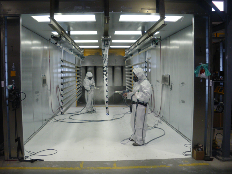 Two DekSmart staff in white PPE powder coating a set of aluminium railings in the powder coating booth.